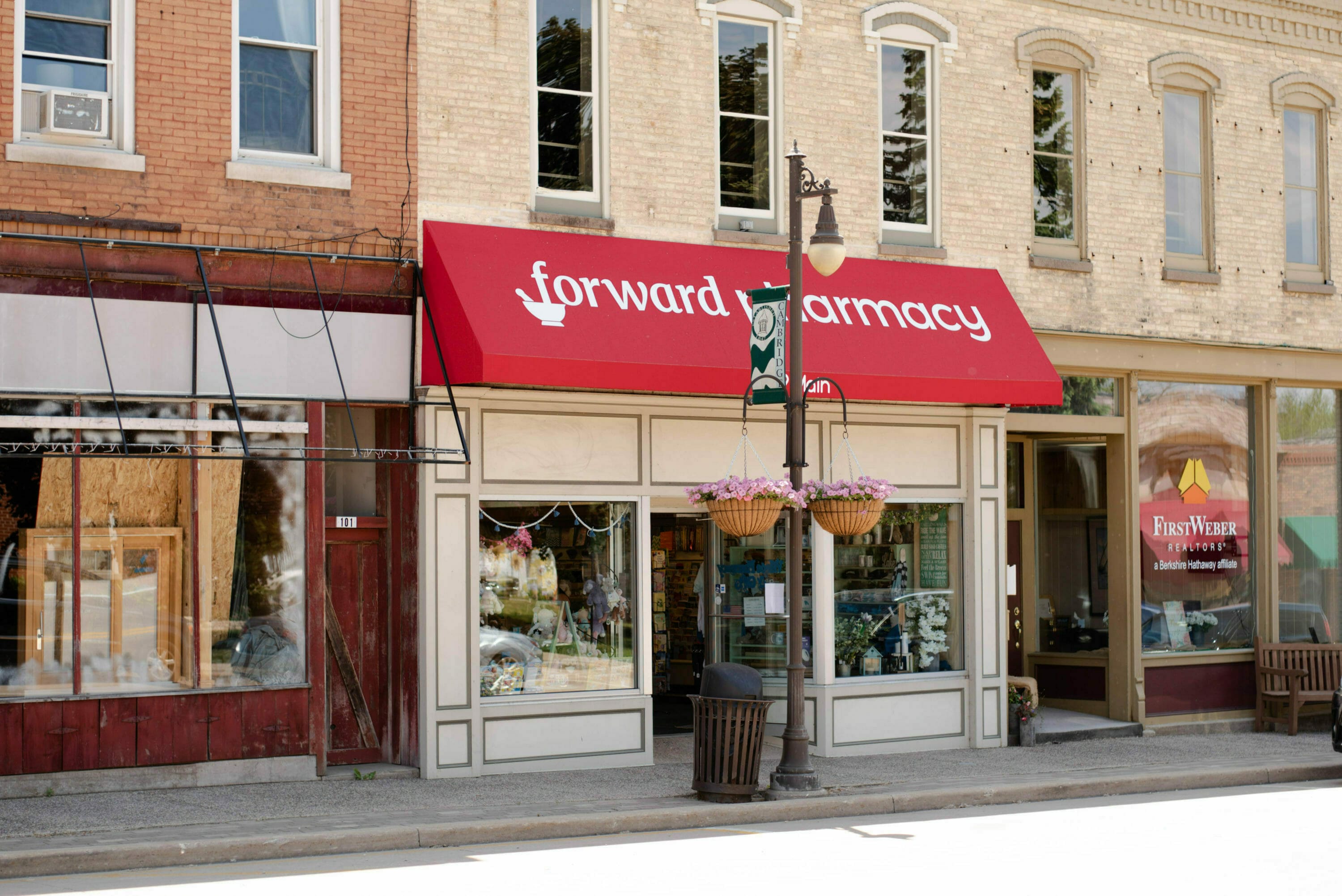 Red awning with "forward pharmacy" signage above a storefront, flanked by a red building and a real estate office.