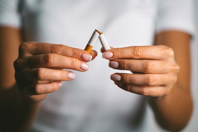 Hands breaking a cigarette in half, symbolizing the act of quitting smoking. Soft focus background enhances the message.