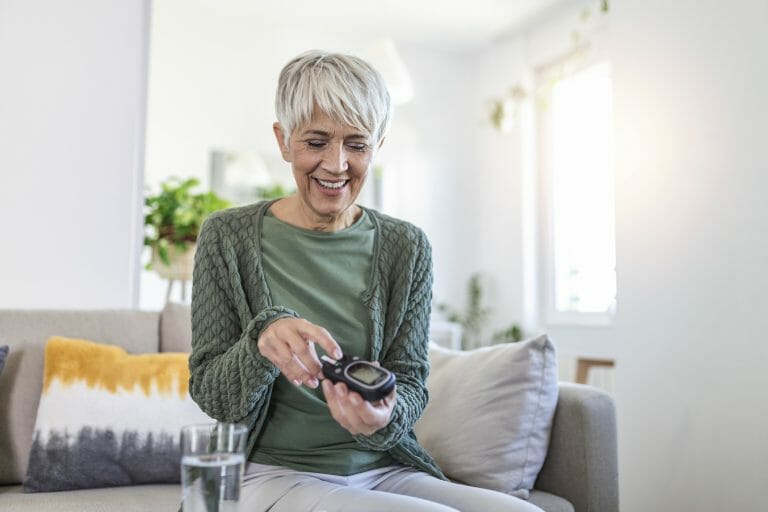 Mature woman with glucometer checking blood sugar level at home.