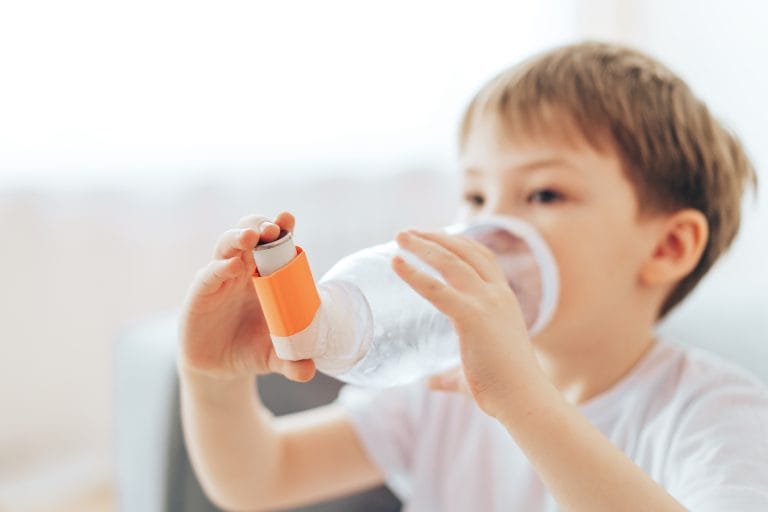 Child holding a water bottle with an orange attachment, focused on drinking, in a bright indoor setting.