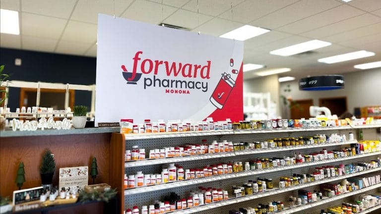 Sign for Forward Pharmacy Monona hangs above shelves stocked with various medications and health products.