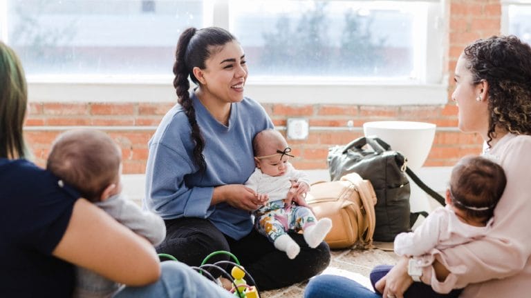 Young adult mother smiles while holding baby at parent support group