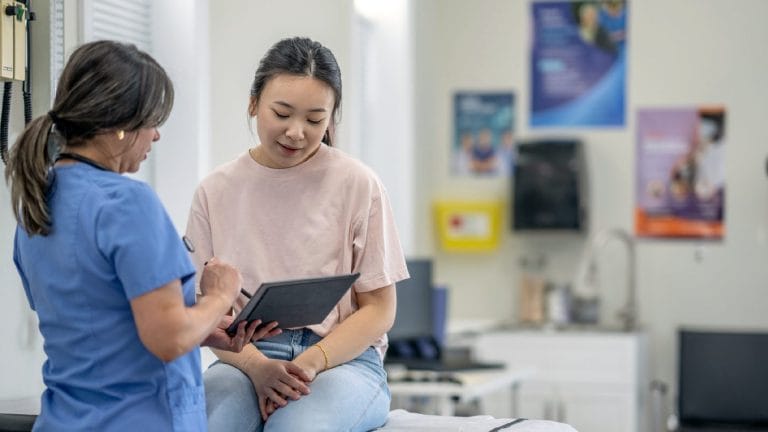 A healthcare professional discusses information on a tablet with a young patient in a medical office setting.
