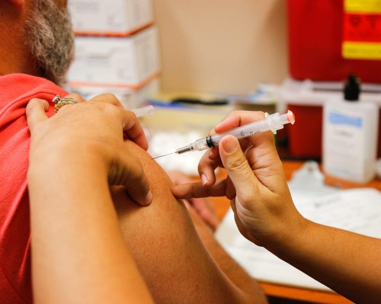 A healthcare worker administers a vaccine to a patient's upper arm in a clinical setting.