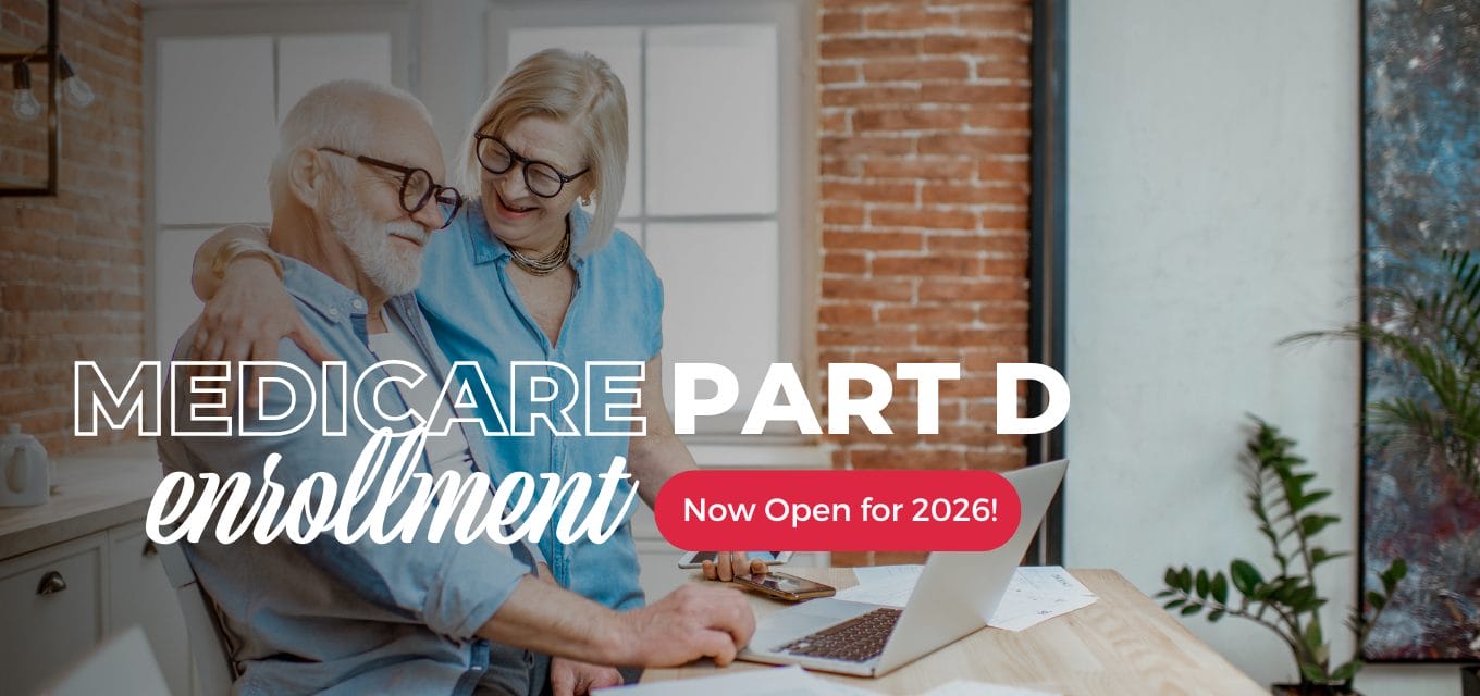A smiling elderly couple discusses Medicare Part D enrollment at a desk with a laptop and plants in a cozy setting.